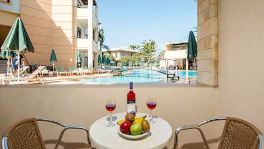 Bildet viser et bord med frukt og vin foran et svømmebasseng og en bygning. (AI-generert tekst)