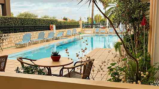 Bilde av et utendørsbasseng med solsenger og bord med en blomsterpotte. (AI-generert tekst)