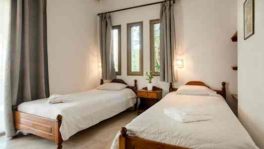 Et rom med to enkeltsenger, et nattbord mellom, hvite sengeklær og grå gardiner over vinduene. (AI-generert tekst)