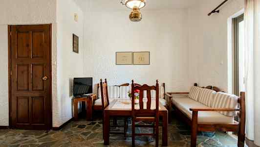 Et rom med et trebord og stoler, en sofa samt en dør og en TV på et trebord. (AI-generert tekst)