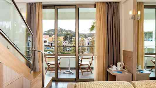 Hotellrom med en balkong med utsikt over omgivelsene. Trapp fører til et øvre nivå. En liten sittegruppe finnes på balkongen. (AI-generert tekst)