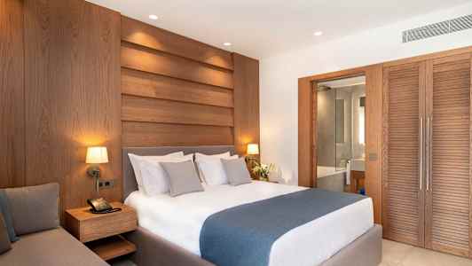 Et hotellrom med en dobbeltseng, trepaneler på veggen og en skyvedør som fører til badet. (AI-generert tekst)