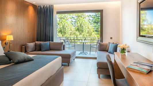 Moderne rom med seng, skrivebord og sittegruppe, utsikt mot terrasse med grønne trær. (AI-generert tekst)