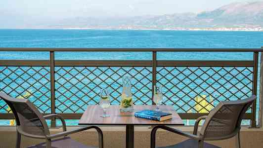 To stoler ved et bord med en karaffel og to glass, med utsikt over havet. (AI-generert tekst)