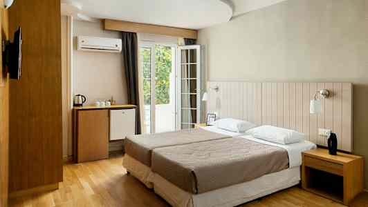 Et hotellrom med to enkeltsenger, skrivebord, minibar og fransk balkong. (AI-generert tekst)