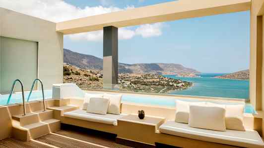 Terrasse med sitteplasser ved basseng med utsikt over havet og fjell. (AI-generert tekst)