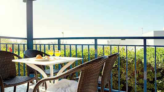 Terrasse med bord og fire rottingstoler, utsikt mot grøntområder og blå himmel. (AI-generert tekst)