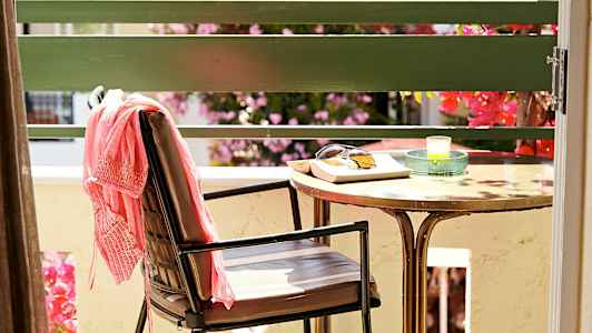 En stol med et rosa klesplagg, et bord med solbriller, en bok og et lys står på en terrasse. (AI-generert tekst)
