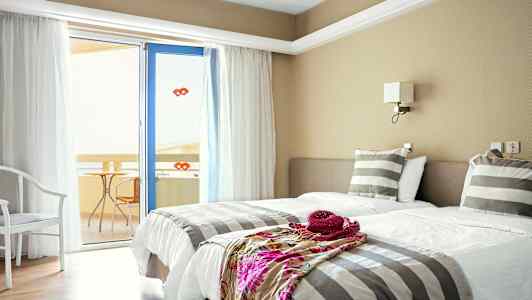 Et hotellrom med to enkeltsenger, stripete sengetøy og en dør til en balkong. (AI-generert tekst)