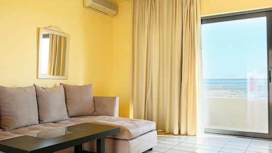 En stue med beige hjørnesofa, glassbord, speil på veggen og stor vindusdør med gardiner og utsikt. (AI-generert tekst)