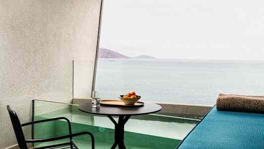 En terrasse med bord, stol og en sitteplass ved et lite basseng med utsikt over havet. (AI-generert tekst)