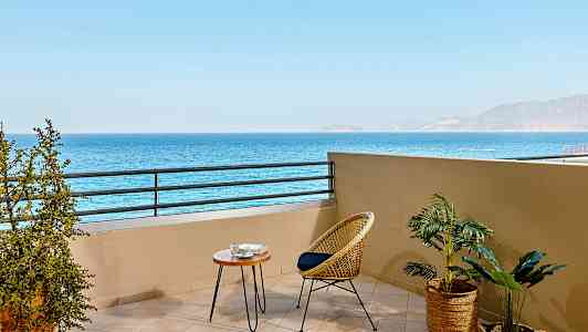 Balkong med utsikt over havet, møblert med en rottingstol og et lite bord. (AI-generert tekst)