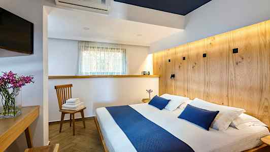 Bilde av et soverom med en dobbeltseng og blå detaljer, et trebord, en stol med håndklær og en TV. (AI-generert tekst)