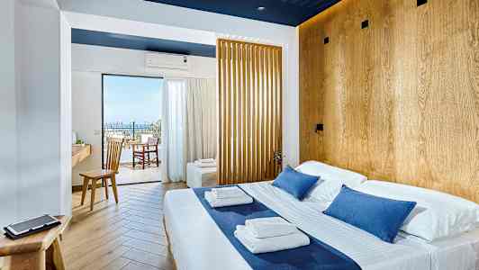 Lyst hotellrom med dobbeltseng og tredetaljer, utsikt mot balkong og hav. (AI-generert tekst)