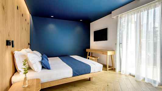 Et moderne hotellrom med blå vegger, en seng med blå sengetepper og treinteriør. (AI-generert tekst)
