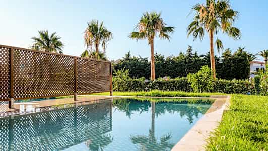 Utendørsbasseng med speilede palmer og gjerde. (AI-generert tekst)