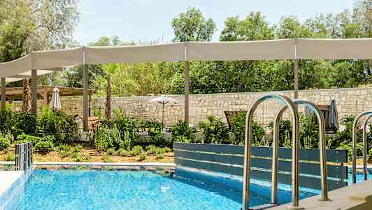 Utendørsbasseng med omkringliggende grønne områder og sitteplasser med skyggeoverbygg. (AI-generert tekst)