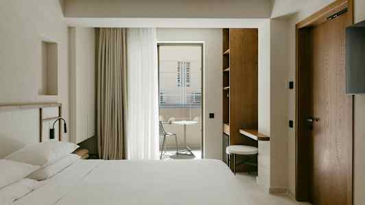 Et hotellrom med en dobbeltseng, skrivebord og balkong med utemøbler. (AI-generert tekst)