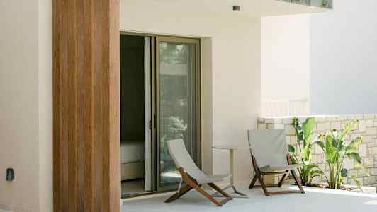 En terrasse med to stoler, et lite bord og grønne planter ved en glassdør. (AI-generert tekst)