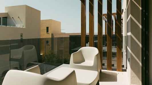 To hvite stoler og et bord på en balkong med glassrekkverk og trepaneler. (AI-generert tekst)