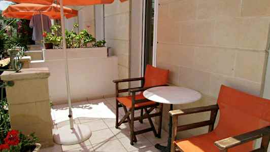 Utendørsterrasse med to oransje stoler og et hvitt bord under en parasoll. (AI-generert tekst)