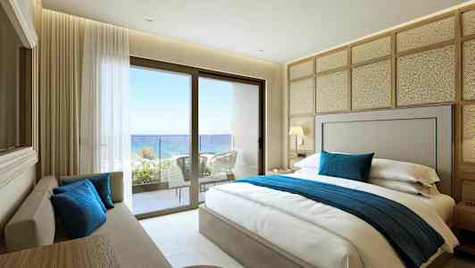 Et hotellrom med en dobbeltseng, sofa og utsikt mot havet fra en balkong. (AI-generert tekst)