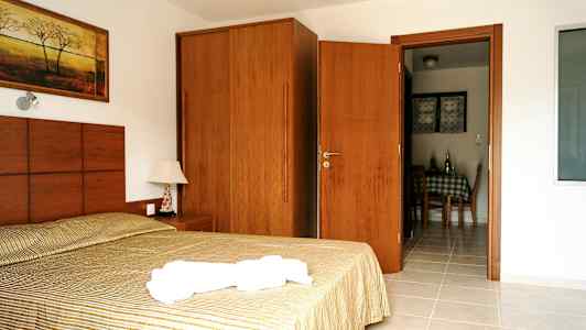 Bilde av et hotellrom med en seng, et nattbord, et skap og en dør som fører til spiseområdet. (AI-generert tekst)