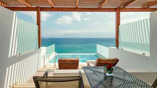 Utsikt over en terrasse med to solsenger, et bord og et privat basseng, med havet i bakgrunnen. (AI-generert tekst)