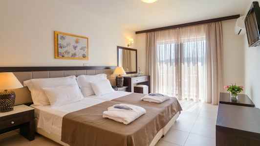 Hotellrom med dobbeltseng, nattbord og store vinduer med lyse gardiner. (AI-generert tekst)