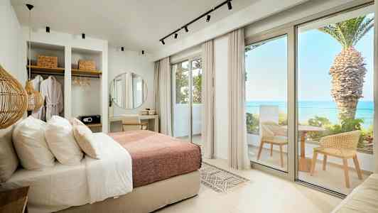 Moderne hotellrom med seng, skrivebord, garderobe og balkong med havutsikt. (AI-generert tekst)