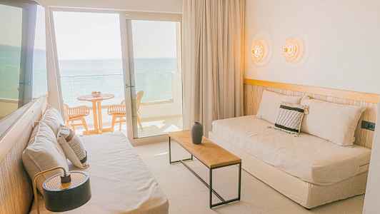 Et hotellrom med sittemøbler og balkong som vender mot havet. (AI-generert tekst)