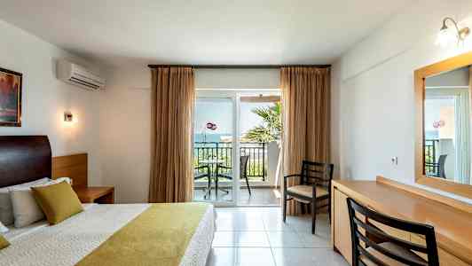 Soverom med dobbeltseng og utsikt mot en balkong med stoler og bord. (AI-generert tekst)