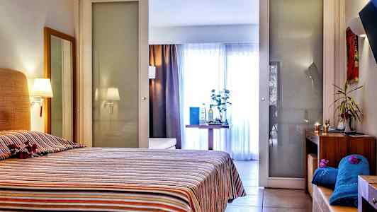 Et hotellrom med en seng med stripet sengeteppe. Rommet har også et bord med dekorative gjenstander og bakgrunn med glassvegger. (AI-generert tekst)