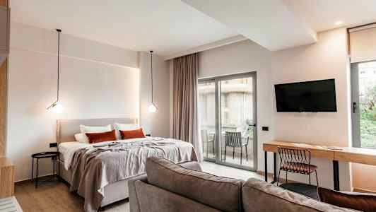 Et moderne hotellrom med seng, sofa, skrivebord, TV og en balkong med utsikt. (AI-generert tekst)