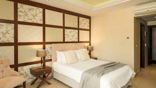 Et hotellrom med en seng, en stol og to nattbord med lamper. (AI-generert tekst)