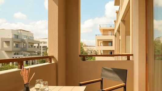 En balkong med bord, stol og utsikt over moderne bygninger. (AI-generert tekst)