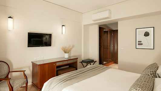 Bilde av et hotellrom med en seng, en TV på veggen, et skrivebord og en lenestol. (AI-generert tekst)