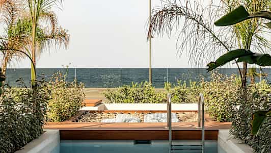 Et lite basseng med en trehage ved siden av, utsikt mot et hav og glassrekkverk. (AI-generert tekst)