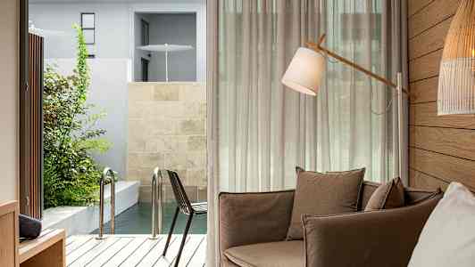 Et rom med en brun lenestol, en gulvlampe og utsikt mot en terrasse med basseng. (AI-generert tekst)