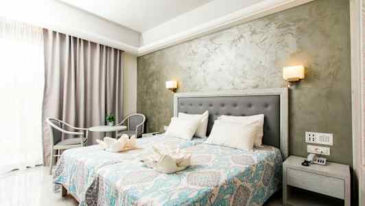 Et hotellrom med dobbeltseng, nattbord, dekorativt sengeteppe og sittegruppe. (AI-generert tekst)