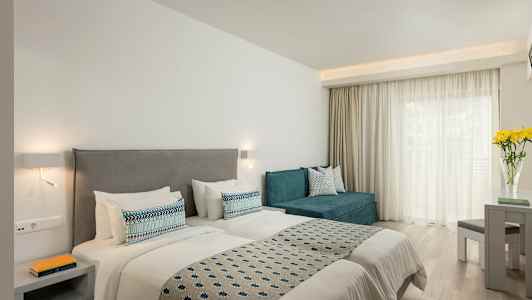 Et hotellrom med to enkeltsenger, en sofa, et bord og blomster på et bord ved et vindu. (AI-generert tekst)