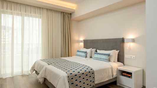 Dobbeltrom med en grå sengegavl, hvitt sengetøy og blåmønstrede puter og sengeteppe, opplyst av vegglamper. (AI-generert tekst)