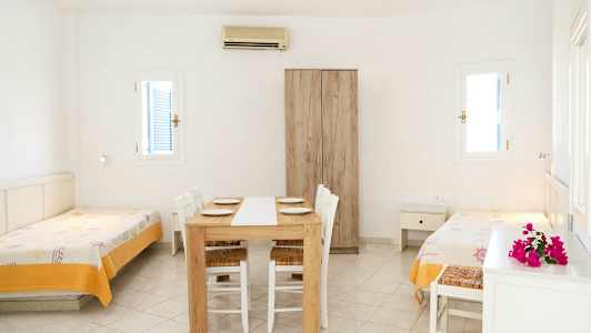 Et lyst rom med to enkeltsenger, et spisebord med stoler og et garderobeskap. (AI-generert tekst)