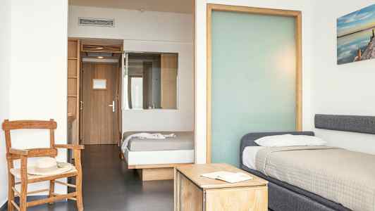 Et hotellrom med to senger, en stol og et bord. (AI-generert tekst)