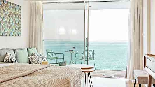 Et soverom med havutsikt gjennom store glassdører som fører til en balkong. (AI-generert tekst)