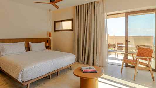 Rom med dobbeltseng, bord og stol, samt glassdør til terrasse. (AI-generert tekst)