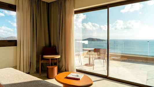 Moderne hotellrom med store glassdører som vender ut mot en balkong med havutsikt. (AI-generert tekst)