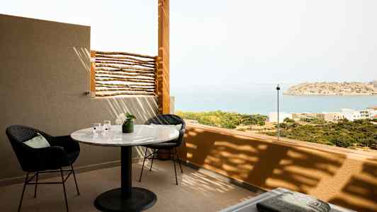 En terrasse med bord, stoler og utsikt over havet og en liten øy. (AI-generert tekst)