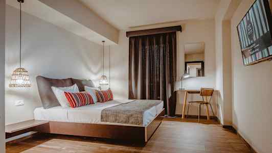 Et hotellrom med en dobbeltseng, skrivebord og stol samt en TV på veggen. (AI-generert tekst)