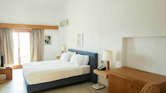 Et hotellrom med en dobbeltseng, skrivebord og balkongdør. (AI-generert tekst)